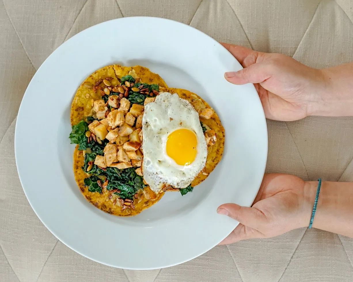 Breakfast on warm corn tortillas, topped with eggs, greens, and golden seared bites
